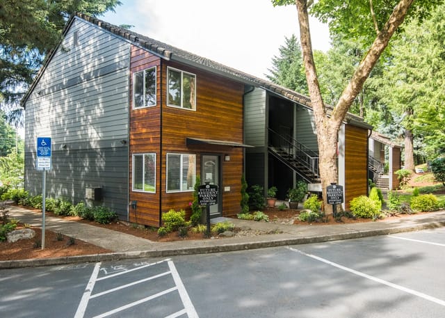 Exterior view of apartment buildings with wood and grey siding, balconies, and parking spaces.