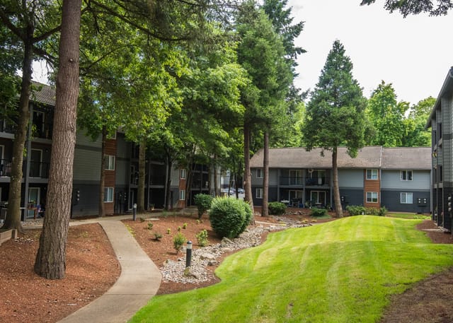 Apartment buildings surrounded by trees with a walking path and a grassy lawn.