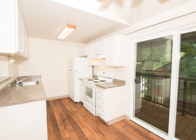 Kitchen with white cabinets and appliances, stainless steel sink, and hardwood floors. Sliding glass door leads to a balcony.