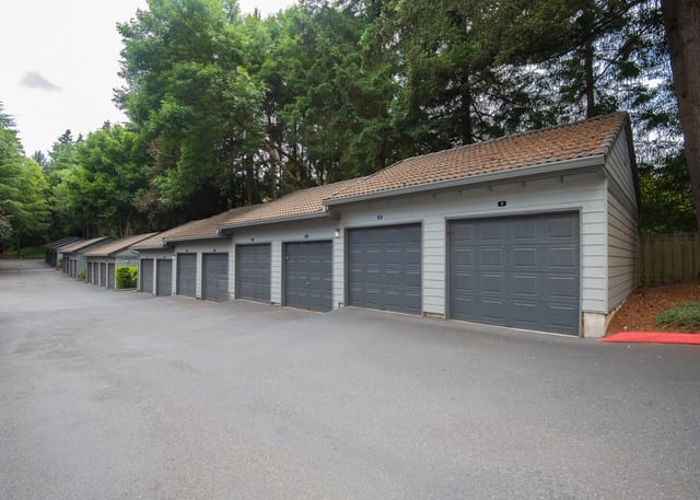 Row of single-car garages with gray doors and green trees in the background.