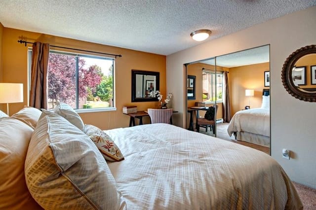 Bedroom with large bed, desk, and mirrored closet doors reflecting another bed.