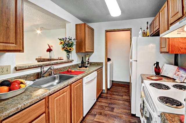 Kitchen with wooden cabinets, granite countertops, stainless steel sink, white dishwasher, and white stove.
