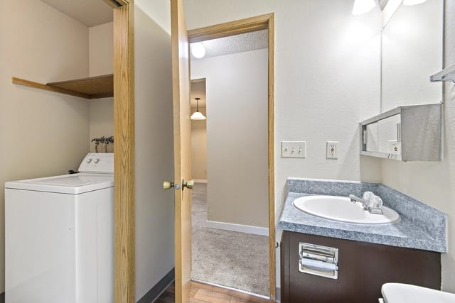 Washer and dryer in laundry closet adjacent to a bathroom vanity with sink and mirror.