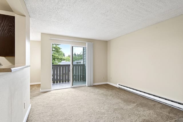 Living room with carpet, beige walls, and a sliding glass door leading to a balcony.