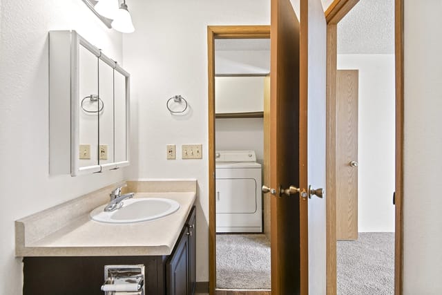 Bathroom with sink, vanity, medicine cabinet, and laundry closet with washer and dryer.