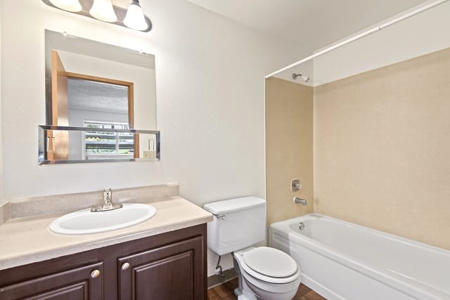 A clean and functional bathroom with a single vanity, toilet, and bathtub with shower.
