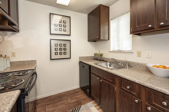 Kitchen with dark wood cabinets, granite countertops, stainless steel sink, and black appliances.