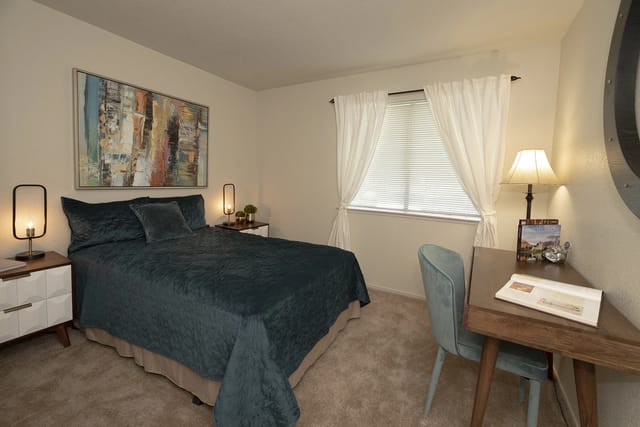 A bedroom featuring a queen-size bed with teal bedding, two nightstands with lamps, and a desk with a chair.