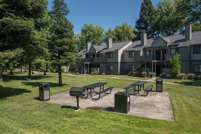 Apartment complex with picnic tables and grills in a grassy courtyard.