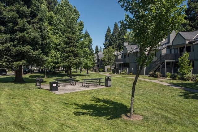 Apartment buildings with picnic tables and grills in a grassy courtyard.
