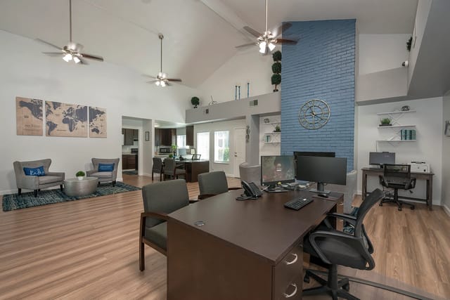 Spacious leasing office with vaulted ceilings, a desk with computers, and a blue brick fireplace.
