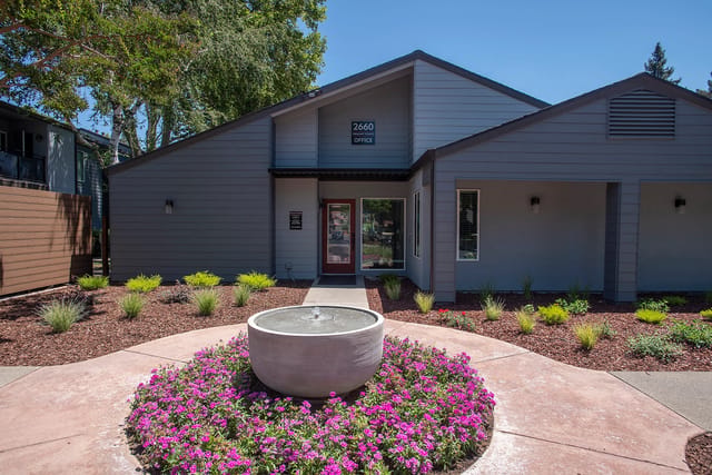 Office building entrance with a fountain and flowers.