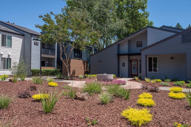 Apartment building exterior with lush landscaping and the office entrance visible.