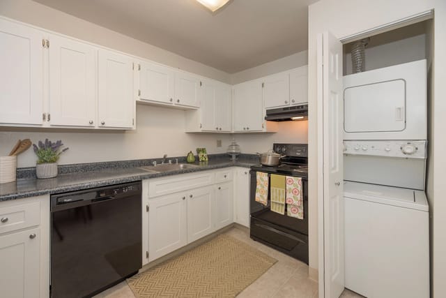 Kitchen with white cabinets, black appliances, and stacked washer/dryer.