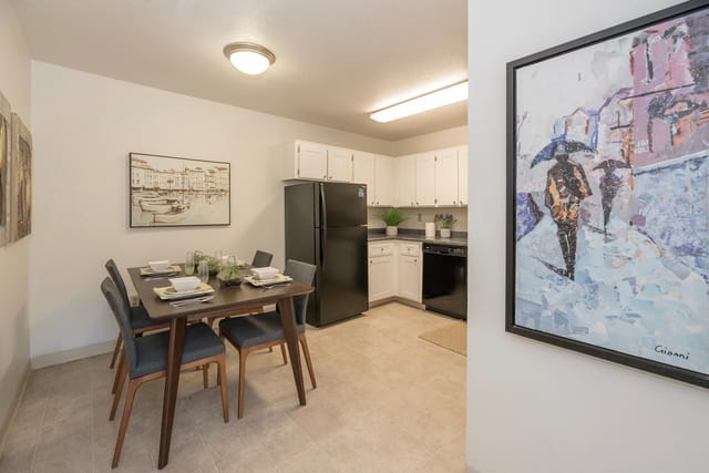 Dining area with a dark wood table and six gray chairs, beside a white-cabinet kitchen with black appliances.