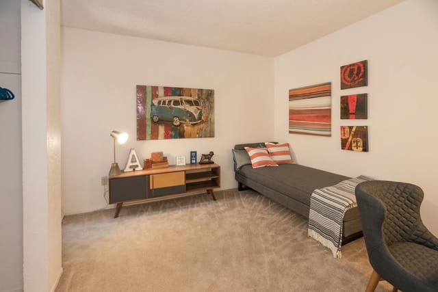 Furnished bedroom in an apartment with a bed, sideboard, chair, and colorful wall art.