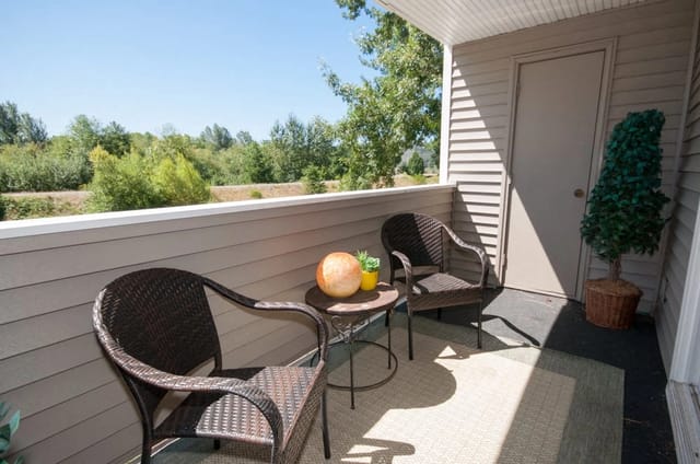 Balcony with two chairs, a table with decorations, and a view of trees.