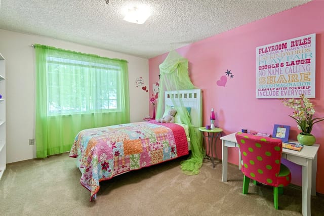 A girl's bedroom with a pink accent wall, a single bed, and a desk.