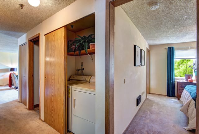 Hallway with stacked washer and dryer, and a glimpse of a bedroom.