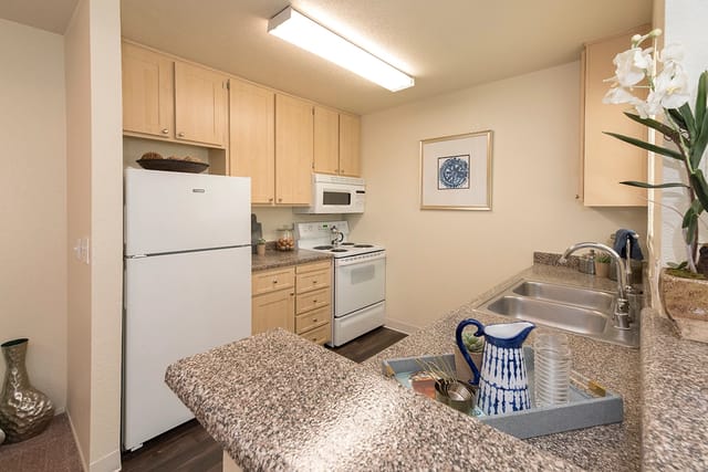 Kitchen in an apartment with beige wooden cabinets, white appliances, and double sink.