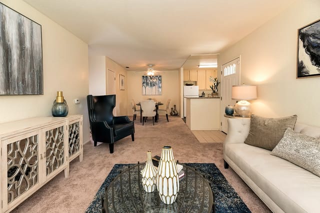 Living room with beige carpet, sofa, armchairs, coffee table, and open kitchen in an apartment.