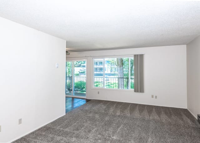 Empty apartment living room with a large window and sliding glass door leading to a balcony.