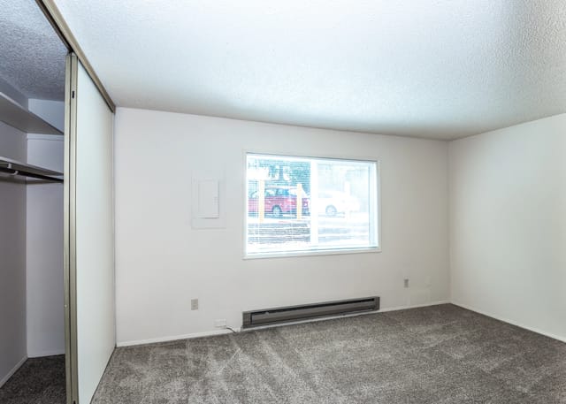 View of an empty bedroom with a sliding door closet and a window showing parked cars.