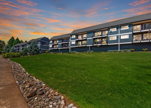 Apartment buildings with balconies and manicured lawns at sunset.
