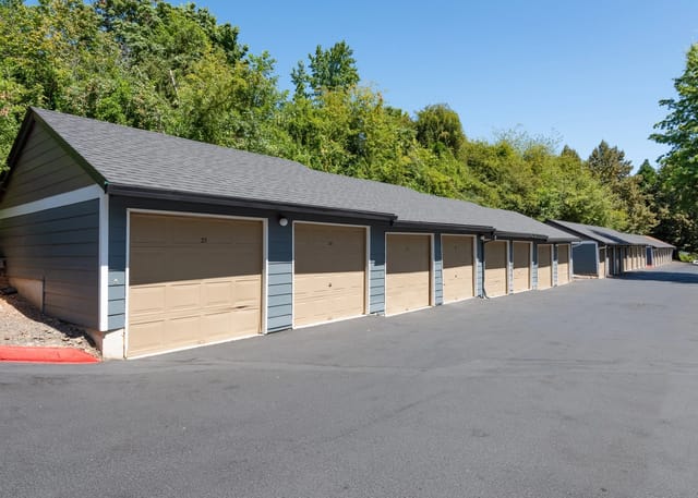 Exterior view of a row of garages with tan doors and blue siding.