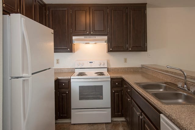 Kitchen with dark wood cabinets, white appliances including a refrigerator, stove, and double sink.