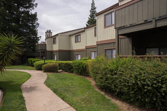 Walkway curving through manicured lawns and hedges alongside apartment buildings.