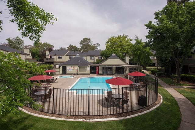 Outdoor swimming pool and hot tub area with tables and umbrellas at an apartment complex.