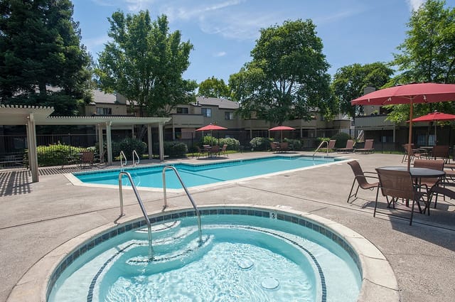 Outdoor swimming pool and spa area with lounge chairs and tables.