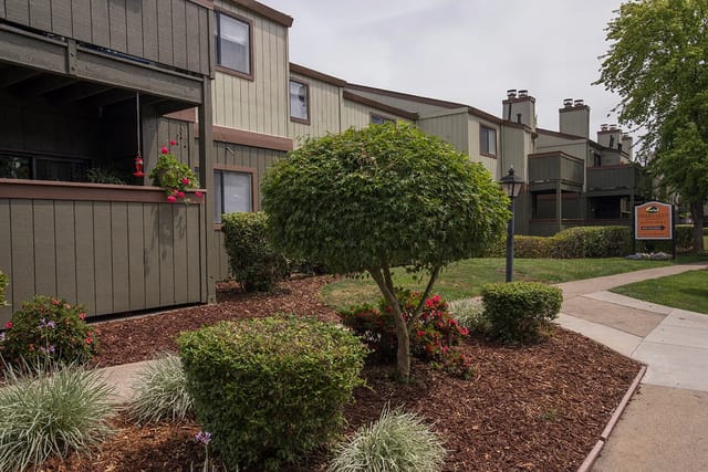 Apartment building exterior with manicured landscaping and a community sign.