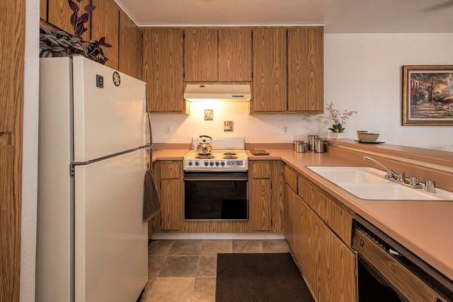 Kitchen with light wood cabinets, beige countertops, white refrigerator, and white stove.