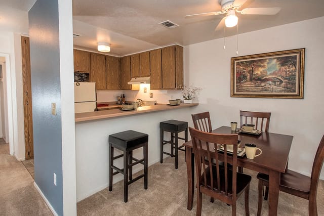 Dining area and kitchen with breakfast bar, stools, and chairs around table.