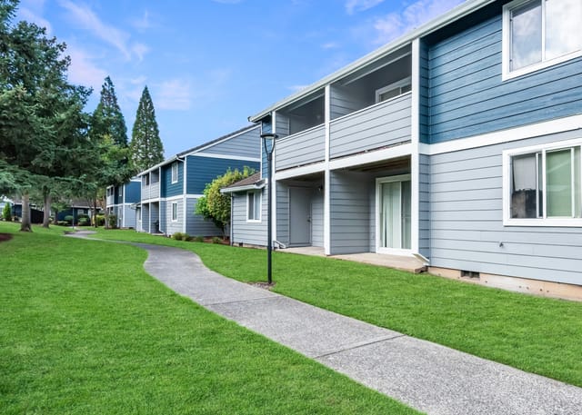 A winding concrete path through a lush green lawn in front of apartment buildings.