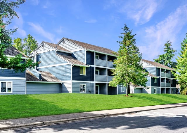 Exterior view of a blue apartment building with balconies and green lawn.