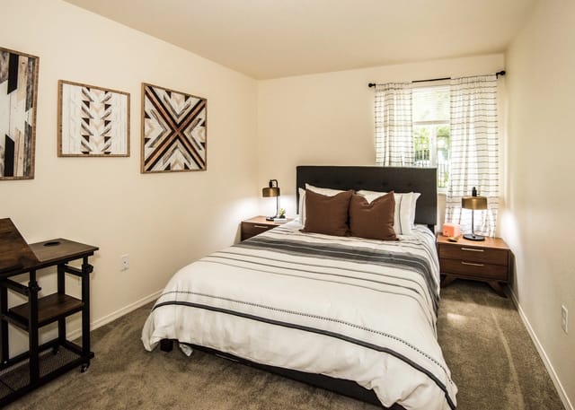 Modern bedroom with queen bed, decorative wall art, and a rolling desk.