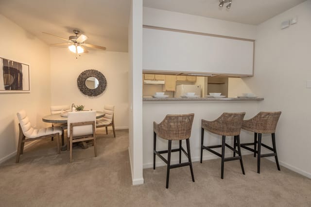 Dining area with a round table and chairs, open to a kitchen with a breakfast bar and stools.