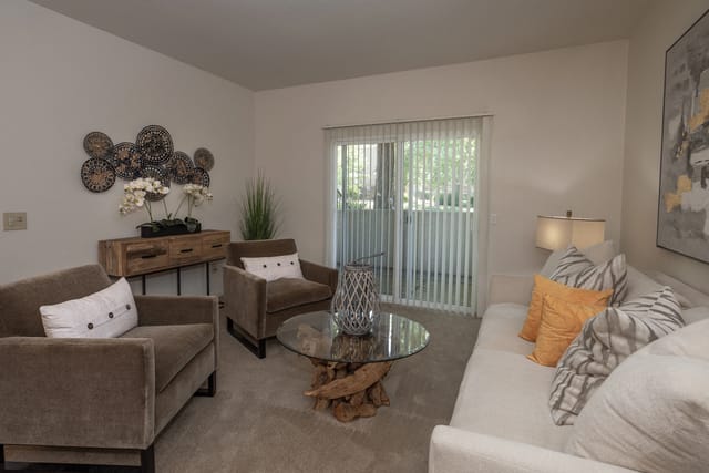 Living room with sofa, accent chairs, coffee table, and balcony access.