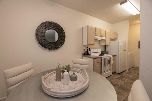 Dining area and kitchen with white appliances, light wood cabinets, and beige walls.