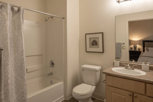 Clean and modern bathroom with a white tub, shower, toilet, and vanity with a mirror.