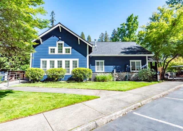 Exterior view of a blue building with white trim and windows, surrounded by green grass and trees.