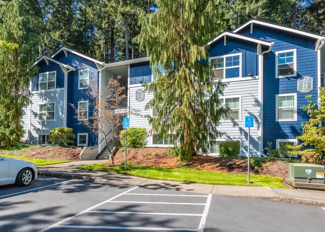 Exterior of apartment building with blue and gray siding and large trees.