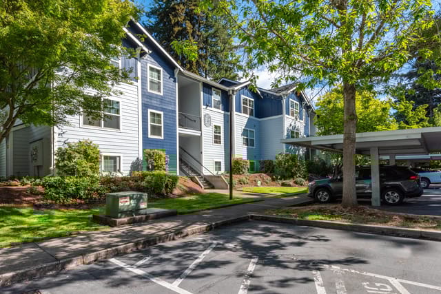 Exterior view of a multi-story apartment building with blue and gray siding and covered parking.
