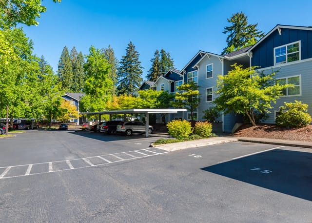 Apartment building exterior with covered parking and trees.