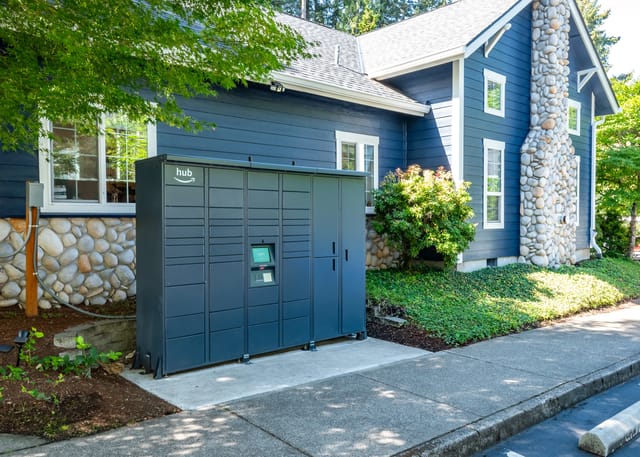 Amazon Hub package locker with the Amazon logo next to a blue building with a stone chimney.