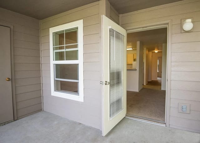 Exterior view of a balcony with a door and window, leading into a hallway and kitchen area.