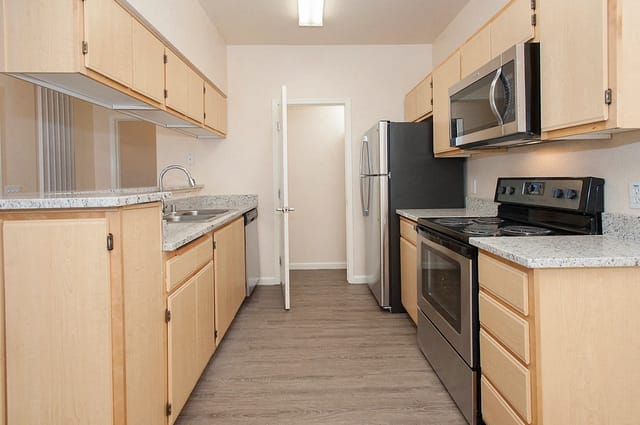 Kitchen with light wood cabinets, granite countertops, stainless steel appliances, and a doorway.
